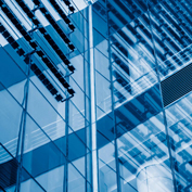 A low-angle shot of a modern skyscraper's blue, reflective glass facade, showing abstract reflections.